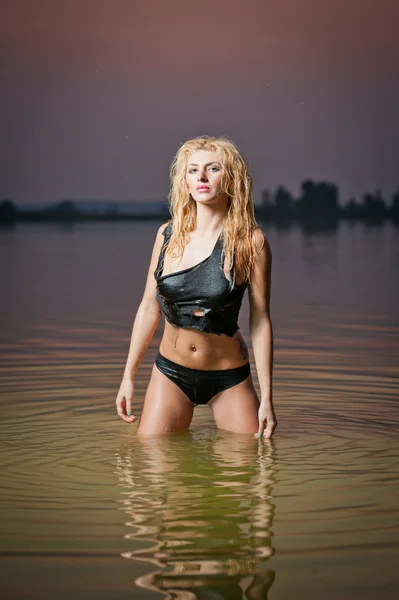 Attractive blonde woman in water at sunset .Beautiful swimsuit model.The beautiful sensual bikini model posing against a setting sun on a body of water .Erotic art photo — Stock Photo, Image