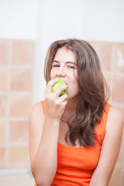 Pretty teen girl eating apple, indoor.Beautiful teenage girl biting an apple .Picture of beautiful teenage biting a green apple — Stock Photo, Image