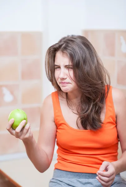 Pretty teen girl in t-shirt concentrated ,hold green fresh apple in hand. Girl holding an green apple indoor, healthy eating — Stock Photo, Image