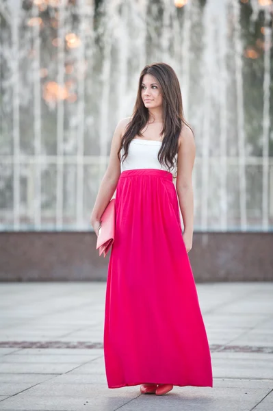Piena lunghezza di giovane femmina caucasica con gonna lunga rossa in piedi di fronte a una fontana in una giornata estiva — Foto Stock