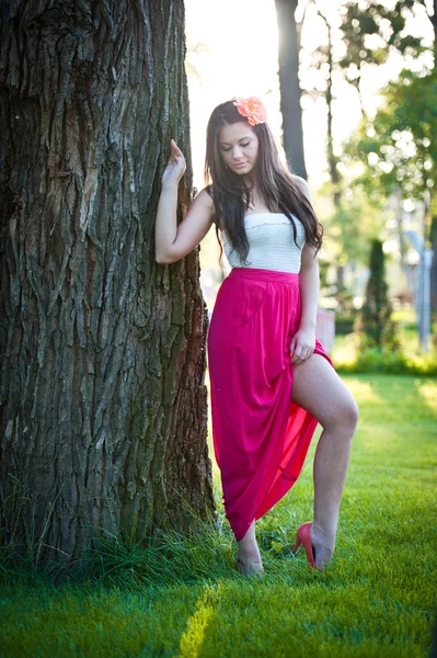 Longitud completa de la joven mujer caucásica con falda larga roja de pie cerca del árbol al aire libre.Retrato romántico de la mujer en el bosque — Foto de Stock