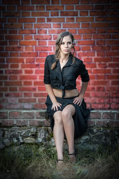 Charming young brunette woman in black dress and high heels near the brick wall.Sexy gorgeous young woman near old wall.Full length portrait of a cute woman with long hair near a brick wall — Stock Photo, Image