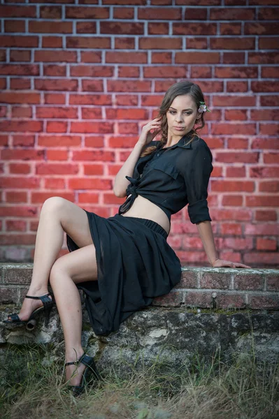 Charmante jeune femme brune en robe noire et talons hauts près du mur de briques.Sexy magnifique jeune femme près de vieux mur.Portrait pleine longueur d'une jolie femme aux cheveux longs près d'un mur de briques — Photo
