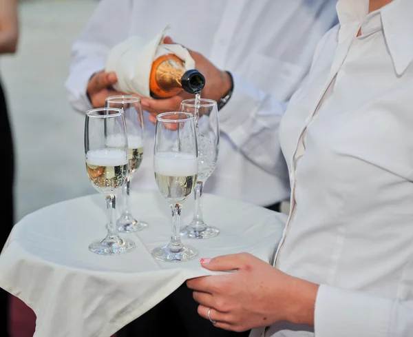 Elegante camarero que vierte champán en copas en un plato. Camarero llenando copas de champán en bandeja — Foto de Stock