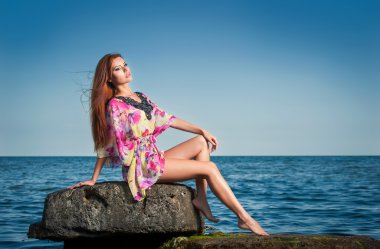 moda portre renkli bir bluz sahilde uzun saçlı genç seksi esmer kız. bir kayanın üzerinde duygusal çekici bir kadın. kadın ile mükemmel bir kayanın üzerinde rahatlatıcı vücut
