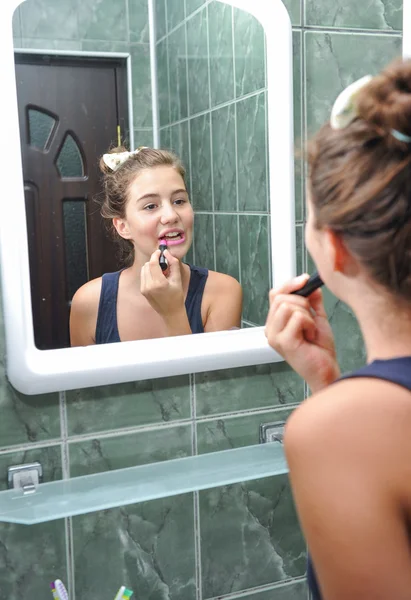 Una hermosa adolescente poniendo lápiz labial y comprobando como se ve. Adolescente chica feliz con su apariencia en el espejo usando lápiz labial . — Foto de Stock