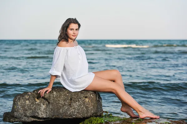 Kaukasisches Teenie-Mädchen im Bikini und weißem Hemd auf Lavafelsen am Meer liegend. Teenager-Mädchen in weißem Hemd auf einem Felsen im Meer sitzend.. — Stockfoto