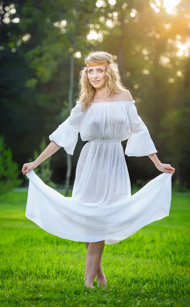 Uma jovem mulher de pé num parque. Menina de poder de flor em um prado. Romântico jovem posando ao ar livre. Mulher atraente em vestido branco longo com um olhar de poder de flor — Fotografia de Stock