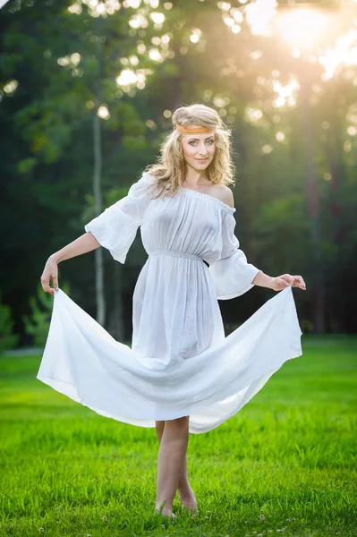 Uma jovem mulher de pé num parque. Menina de poder de flor em um prado. Romântico jovem posando ao ar livre. Mulher atraente em vestido branco longo com um olhar de poder de flor — Fotografia de Stock