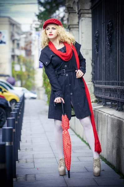 Atractiva joven en una foto de moda de invierno. Hermosa chica joven de moda con paraguas rojo en la calle — Foto de Stock