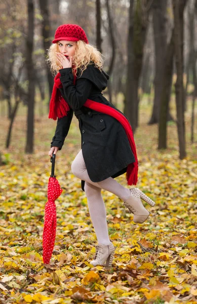 Atractiva joven en una sesión de otoño de moda. Hermosa chica joven de moda con paraguas rojo, gorra roja y bufanda roja en el parque —  Fotos de Stock