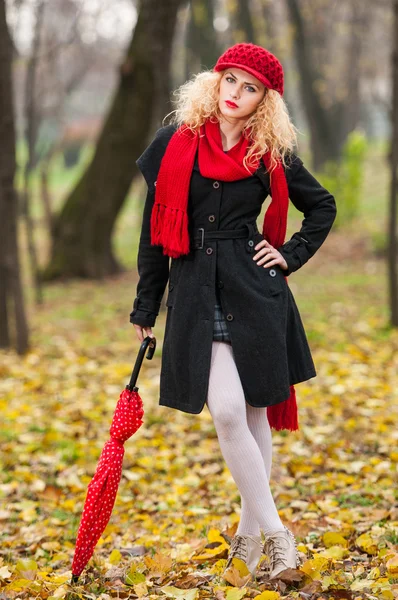 Attrayant jeune femme dans un tournage de mode d'automne. Belle jeune fille à la mode avec parapluie rouge, casquette rouge et écharpe rouge dans le parc — Photo