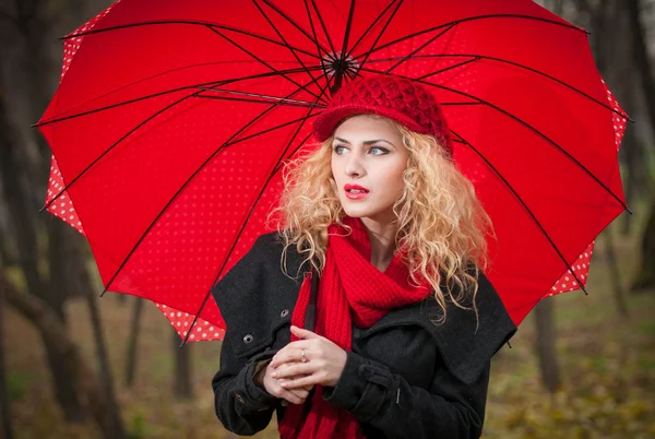 Attraktive junge Frau bei einem Mode-Shooting im Herbst. schönes modisches junges Mädchen mit rotem Regenschirm, roter Mütze und rotem Schal im Park. — Stockfoto