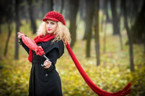 Attraente giovane donna in un servizio fotografico di moda autunno. Bella ragazza alla moda con ombrello rosso, berretto rosso e sciarpa rossa nel parco . — Foto Stock