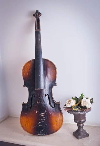 Velho violino encostado à parede perto de um vaso com rosas — Fotografia de Stock