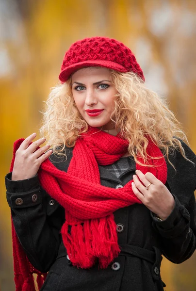 Attraente giovane donna in un servizio fotografico di moda autunno. Bella ragazza alla moda con berretto rosso e sciarpa rossa nel parco. Donne bionde con accessori rossi in posa all'aperto. Bella ragazza dai capelli biondi — Foto Stock