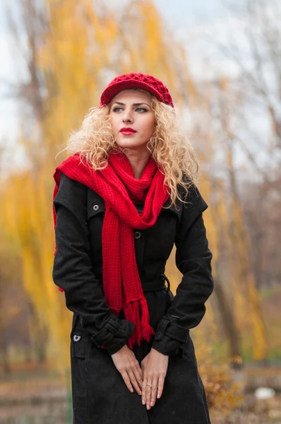 Jovem atraente em uma sessão de moda de outono. Menina bonita e elegante com boné vermelho e cachecol vermelho no parque. Mulheres loiras com acessórios vermelhos posando ao ar livre. Menina de cabelo claro agradável — Fotografia de Stock