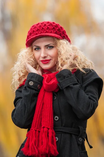 Привлекательная молодая женщина на осенней фотосессии. Модная молодая девушка в красной шапке и красном шарфе в парке. Блондинки с красными аксессуарами на открытом воздухе. Красивая светлая девушка — стоковое фото