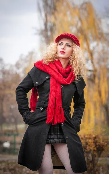 Attraente giovane donna in un servizio fotografico di moda autunno. Bella ragazza alla moda con berretto rosso e sciarpa rossa nel parco. Donne bionde con accessori rossi in posa all'aperto. Bella ragazza dai capelli biondi — Foto Stock