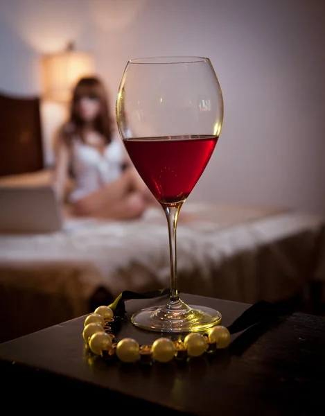 Mysterious lady staying in bed working on laptop with a glass of wine and a rope of golden pearls foreground. Sensual woman on bed and glass of wine. Beautiful girl indoor relaxation moments — Stock Photo, Image