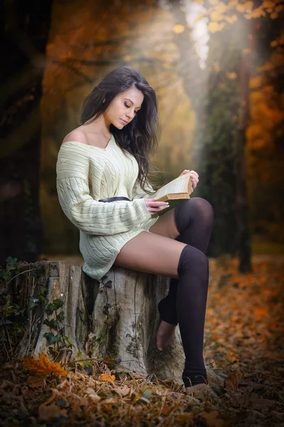 Young Caucasian sensual woman reading a book in a romantic autumn scenery. Portrait of pretty young girl in the forest in autumn day. Fashion portrait of a beautiful young woman in autumn forest — Stock Photo, Image