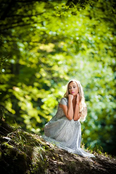 Lovely young lady wearing elegant white dress enjoying the beams of celestial light on her face in enchanted woods. Pretty blonde fairy lady with white dress. Glamorous princess in the woods — Stock Photo, Image