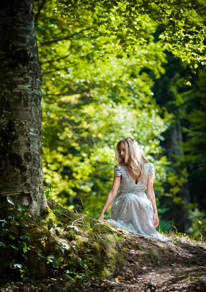 Lovely young lady wearing elegant white dress enjoying the beams of celestial light on her face in enchanted woods. Pretty blonde fairy lady with white dress. Glamorous princess in the woods — Stock Photo, Image