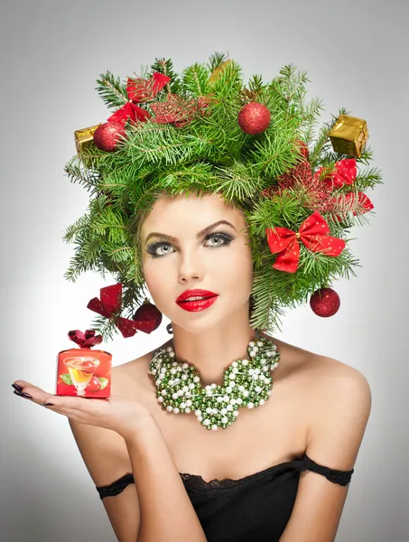 Hermoso maquillaje creativo de Navidad y el estilo de pelo de la sesión de interior. Chica modelo de moda de belleza. El invierno. Hermosa chica atractiva con accesorios de árbol de Navidad en el estudio sosteniendo un regalo . — Foto de Stock