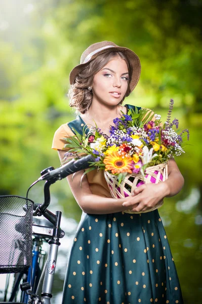 Beautiful girl with cute hat and basket with flowers having fun in park with bicycle. Healthy outdoor lifestyle concept. Vintage scenery. Pretty blonde girl with retro look with bike — Stock Photo, Image