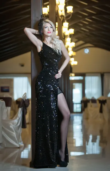 Молодая красивая роскошная женщина в длинном элегантном черном платье. Красивая молодая блондинка с яркими огнями на заднем плане. Соблазнительная блондинка в роскошном особняке, винтажный стиль — стоковое фото