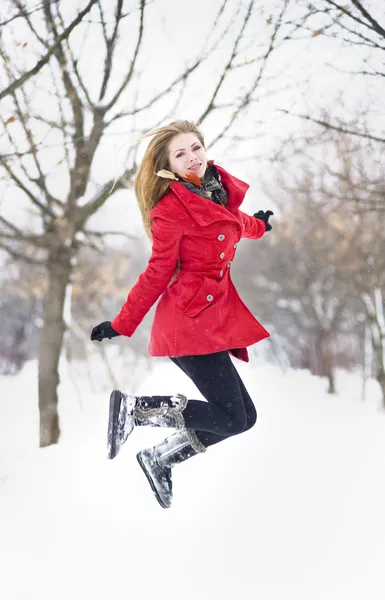 Atractiva chica rubia con guantes, abrigo rojo y sombrero rojo posando en la nieve de invierno. Hermosa mujer en el paisaje de invierno. Mujer joven en invierno al aire libre —  Fotos de Stock