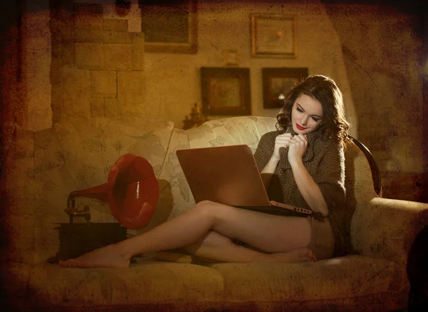 Beautiful young woman sitting on bed working on laptop having a red gramophone near her, in boudoir scenery. Attractive brunette girl with long hair and long legs laying down on bed with a laptop — Stock Photo, Image