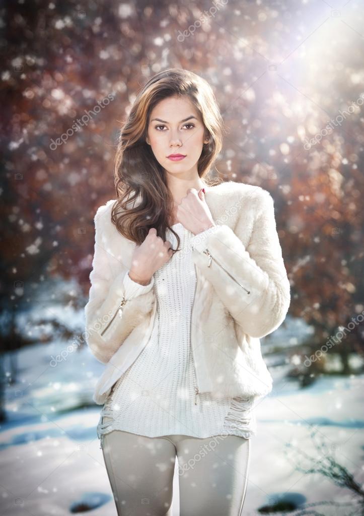 Portrait of young beautiful woman wearing white clothes outdoor. Beautiful brunette girl with long hair posing outdoor in a cold winter day. Beautiful fashionable young woman in winter scenery.