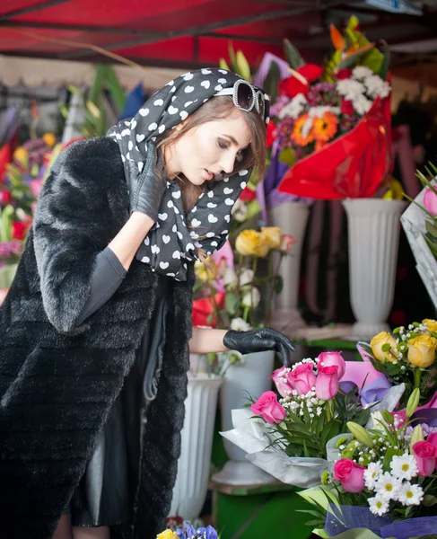 Mooie brunette vrouw met handschoenen bloemen in de winkel van de bloemist te kiezen. modieuze vrouw met zonnebril en hoofd sjaal op bloemenwinkel. mooie brunette in zwart-wit bloemen - stedelijke schot kiezen — Stockfoto