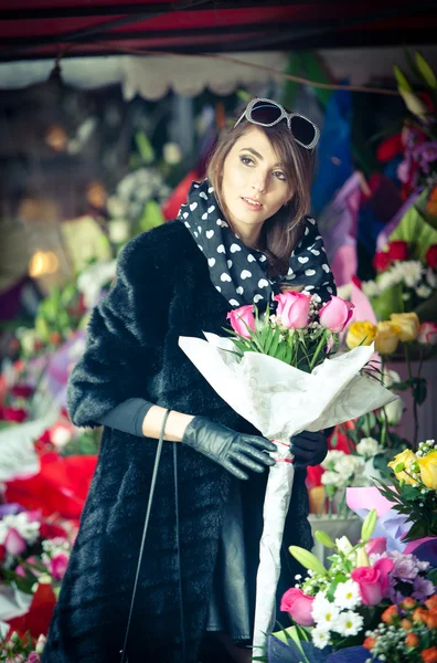 Mulher morena bonita com luvas escolhendo flores na florista. Feminino na moda com óculos de sol e lenço de cabeça na loja de flores. Morena bonita em preto escolhendo flores - tiro urbano — Fotografia de Stock