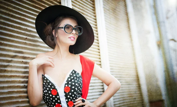 Chica morena atractiva con sombrero negro, bufanda roja y gafas de sol posando al aire libre. Hermosa mujer joven de moda con accesorios modernos, tiro urbano. Hermosa morena con gran sombrero negro sonriendo . — Foto de Stock