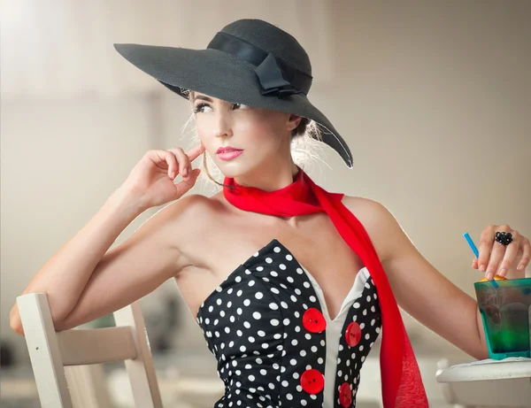 Señorita atractiva de moda con sombrero negro y bufanda roja sentado en la silla en el restaurante, tiro interior. Mujer joven posando en un paisaje elegante. Foto de arte de mujer sensual elegante, estilo vintage —  Fotos de Stock