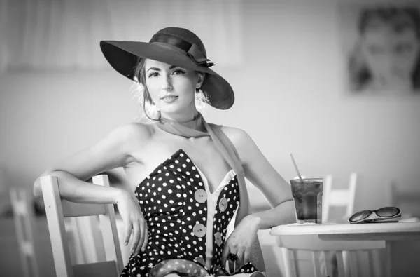 Fashionable attractive lady with hat and scarf sitting in restaurant, indoor shot. Young woman posing in elegant scenery, black and white. Art photo of elegant sensual woman relaxing, vintage style — Stock Photo, Image