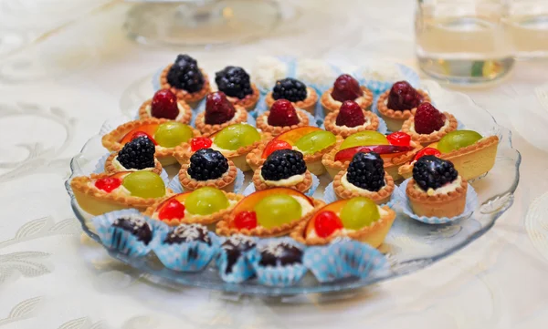 Set of tasty mini cakes with raspberries, blackberries, cranberries, blueberries and grapes on white table. Wedding decoration with mini tarts with various berries. Arrangement with mini tarts. — Stock Photo, Image