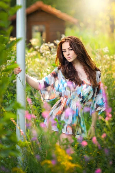 Joven hermosa mujer de pelo rojo en blusa multicolor en un día soleado. Retrato de atractiva mujer de pelo largo en medio de flores silvestres, tiro al aire libre. Chica bonita disfrutando de la naturaleza en verano — Foto de Stock