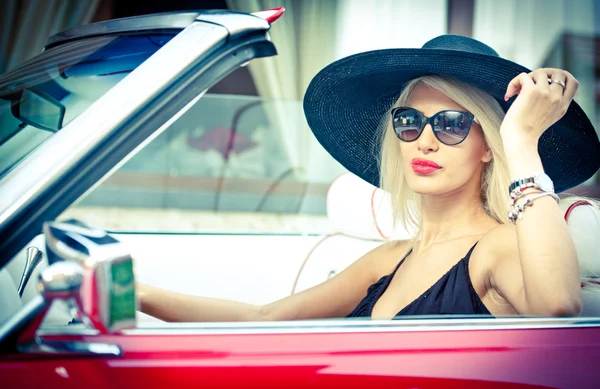 Buiten zomer portret van stijlvolle blonde vintage vrouw een converteerbare Rode retro auto rijden. modieuze aantrekkelijke eerlijke haar teef met zwarte hoed in rode voertuig. zonnige heldere kleuren, buiten schot. — Stockfoto