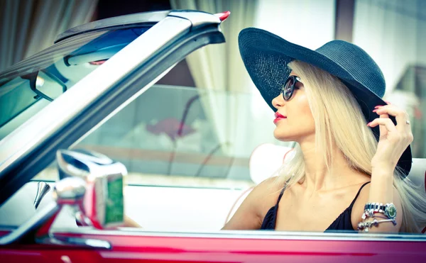 Portrait d'été en plein air d'une femme vintage blonde élégante conduisant une voiture rétro rouge décapotable. Fille attrayante à la mode aux cheveux clairs avec chapeau noir dans un véhicule rouge. Couleurs vives ensoleillées, plan extérieur . — Photo