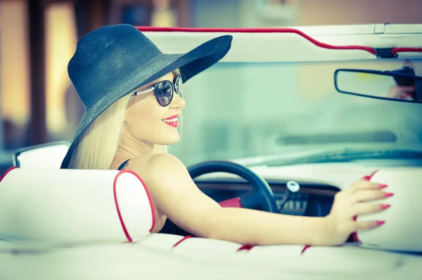 Retrato de verano al aire libre de mujer vintage rubia con estilo conduciendo un coche retro rojo convertible. Moda atractiva hembra de pelo rubio con sombrero negro en vehículo rojo. Soleados colores brillantes, tiro al aire libre . — Foto de Stock