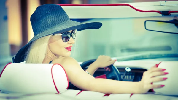 Retrato de verão ao ar livre de mulher vintage loira elegante dirigindo um carro retro vermelho conversível. Mulher de cabelo claro atraente na moda com chapéu preto no veículo vermelho. Sunny cores brilhantes, tiro ao ar livre . — Fotografia de Stock
