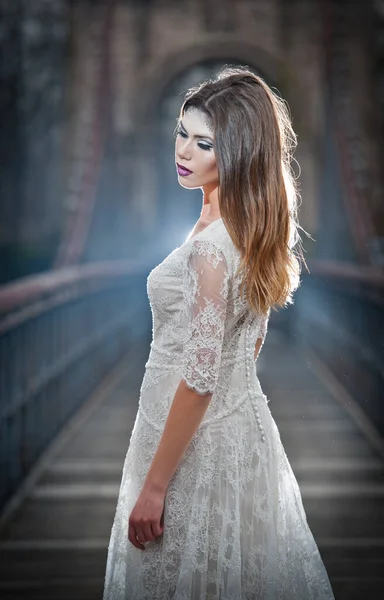 美丽的年轻女子 穿着优雅的白色连衣裙 享受梁天空光和雪花落在她的脸上 在长婚纱冬季风光一座桥上摆姿势的黑发女孩 — 图库照片