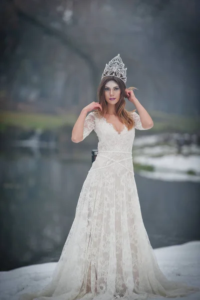 美丽的年轻女子 穿着优雅的白色连衣裙 享受梁天空光和雪花落在她的脸上 在长婚纱冬季风光一座桥上摆姿势的黑发女孩 — 图库照片
