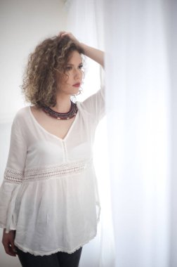 Cılız, genç, kıvırcık saçlı beyaz bluz giyen bir manken. Güneş gözlüklü ve kolyeli güzel, seksi bir kadın resmi.