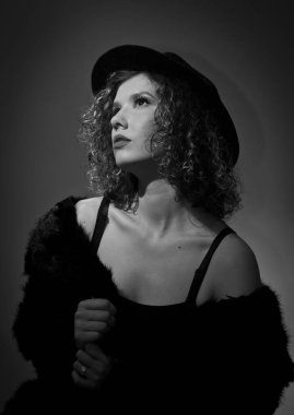 Stüdyoda yeşil bir sandalyede oturan siyah kürklü şık bir mankenin portresi. Siyah külotlu çorap giyen genç ve güzel bir kadın. Siyah şapkalı, sandalyede oturan çekici bir kadının portresi.