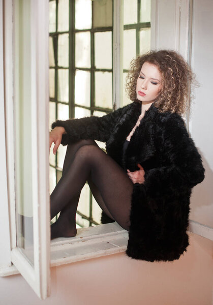 Portrait of a fashionable model with black fur sitting in a green chair in studio. Close up Portrait of young beautiful woman .Portrait of attractive woman sitting in chair isolated on grey background