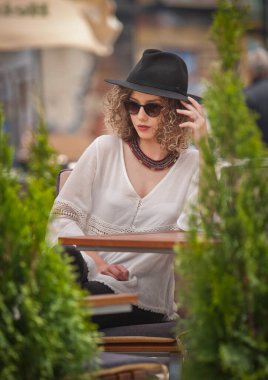 Mutlu esmer kız parkta oturmuş, bir bardak soğuk yeşil suyu iken gülümseyen içine mesafe içme güneş gözlüklü. Genç kadın beyaz bir gömlek giymiş suyu içme tezgah hoş 